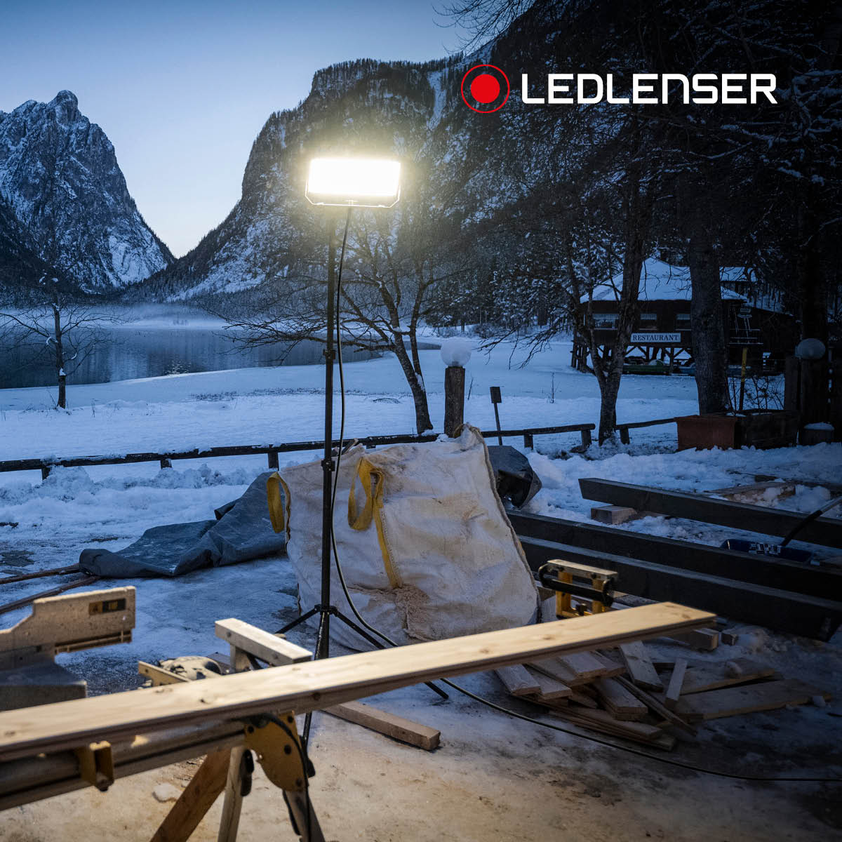Ledlenser floodlight on a tall tripod lighting a snowy outdoor building site at dusk