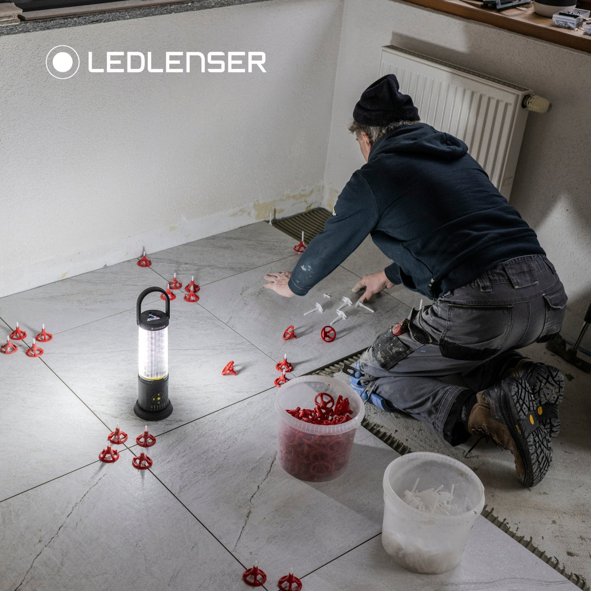 Tiler laying large floor tiles with levelling clips, lit by a Ledlenser AL10R Work standing on the floor