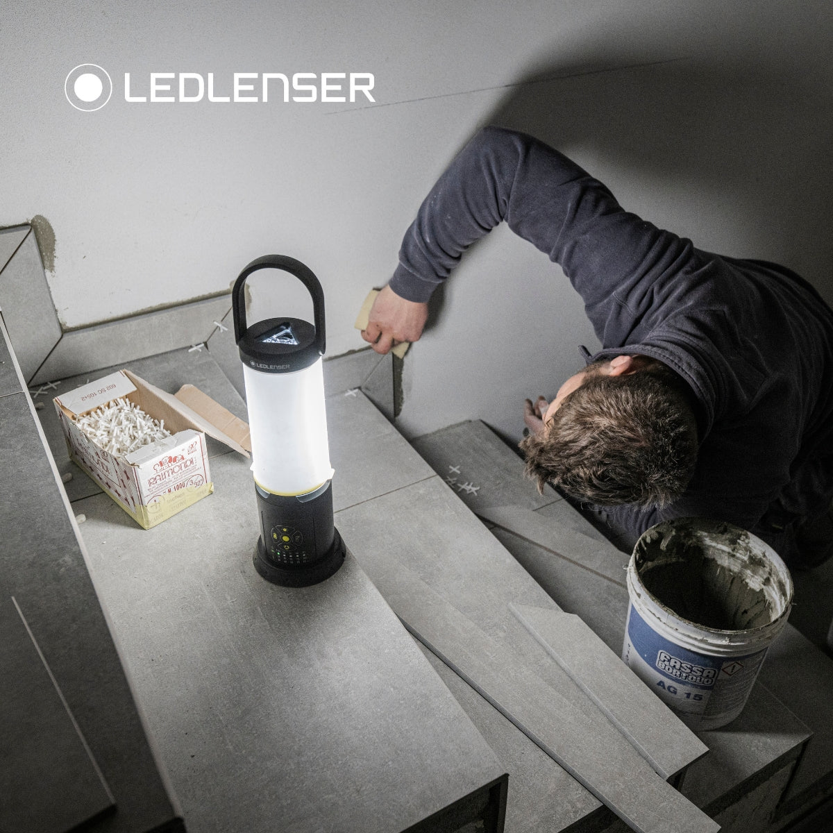 Tiler fixing tiles to a stairway wall, lit by a Ledlenser AL10R Work with diffuser standing on a step