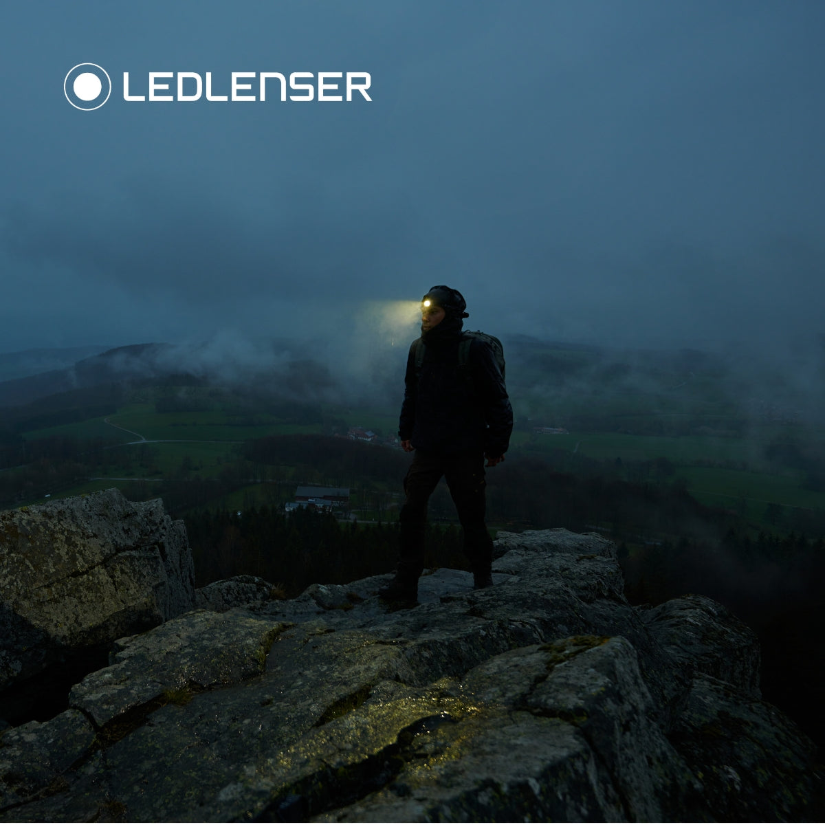 Hiker on a rocky outcrop at dusk wearing the Ledlenser MH10 SE