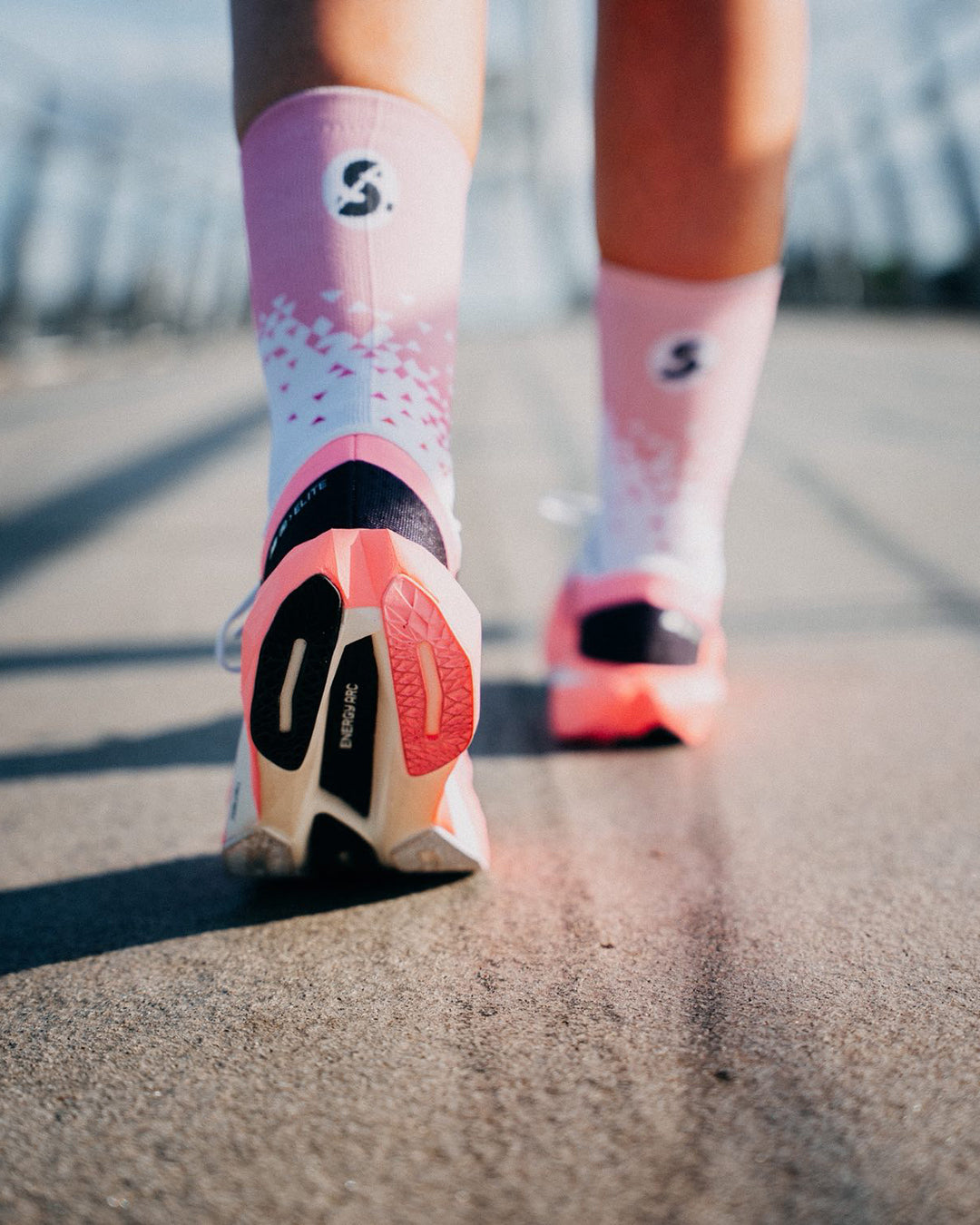 Rear view of a runner on a bridge in Stride Flash Pink running socks, pink cuff with S logo