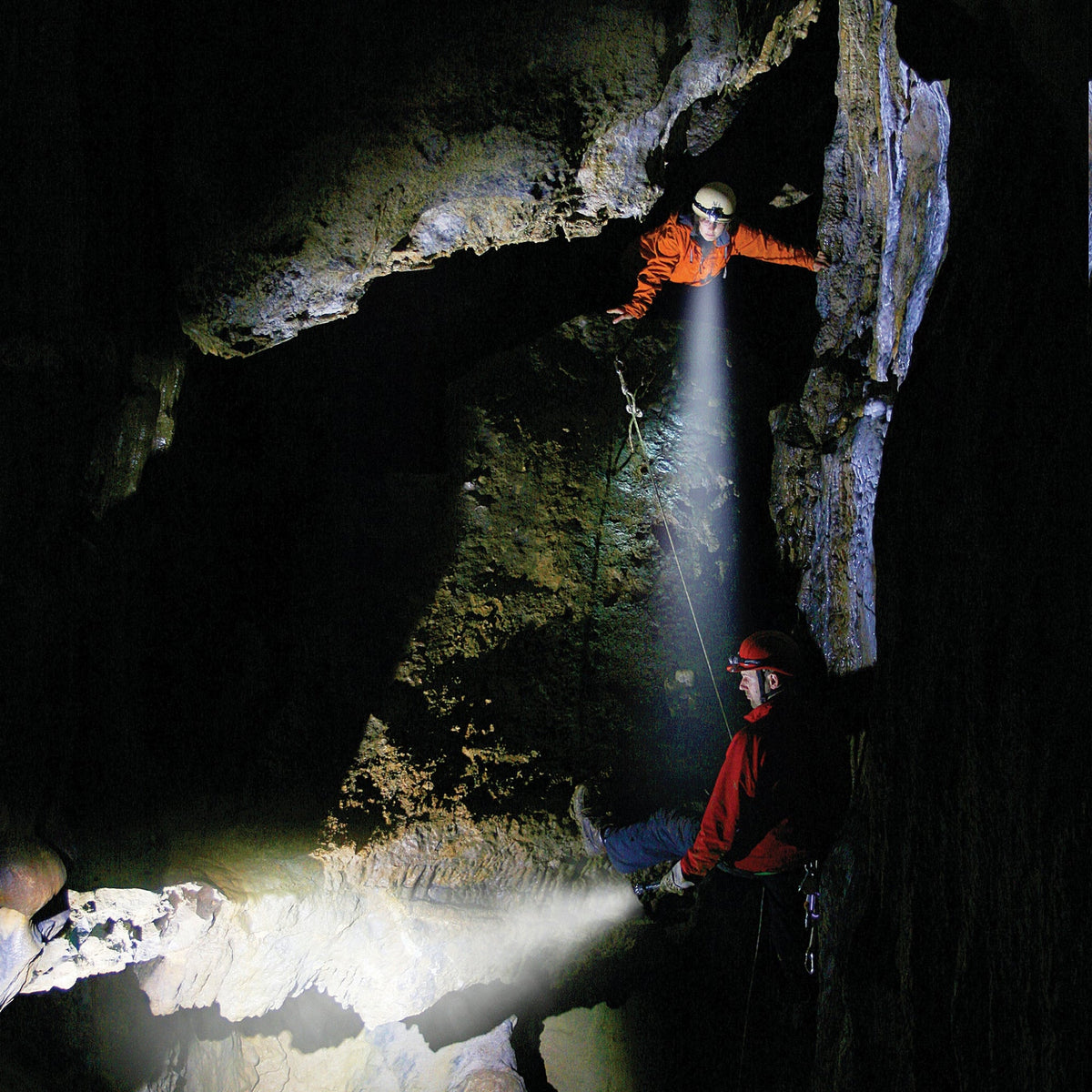 Two cavers in helmets lighting a rock chamber with Ledlenser head torch beams