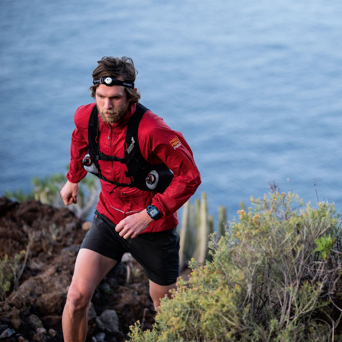 Trail runner in a red jacket climbing a coastal path wearing a Ledlenser head torch