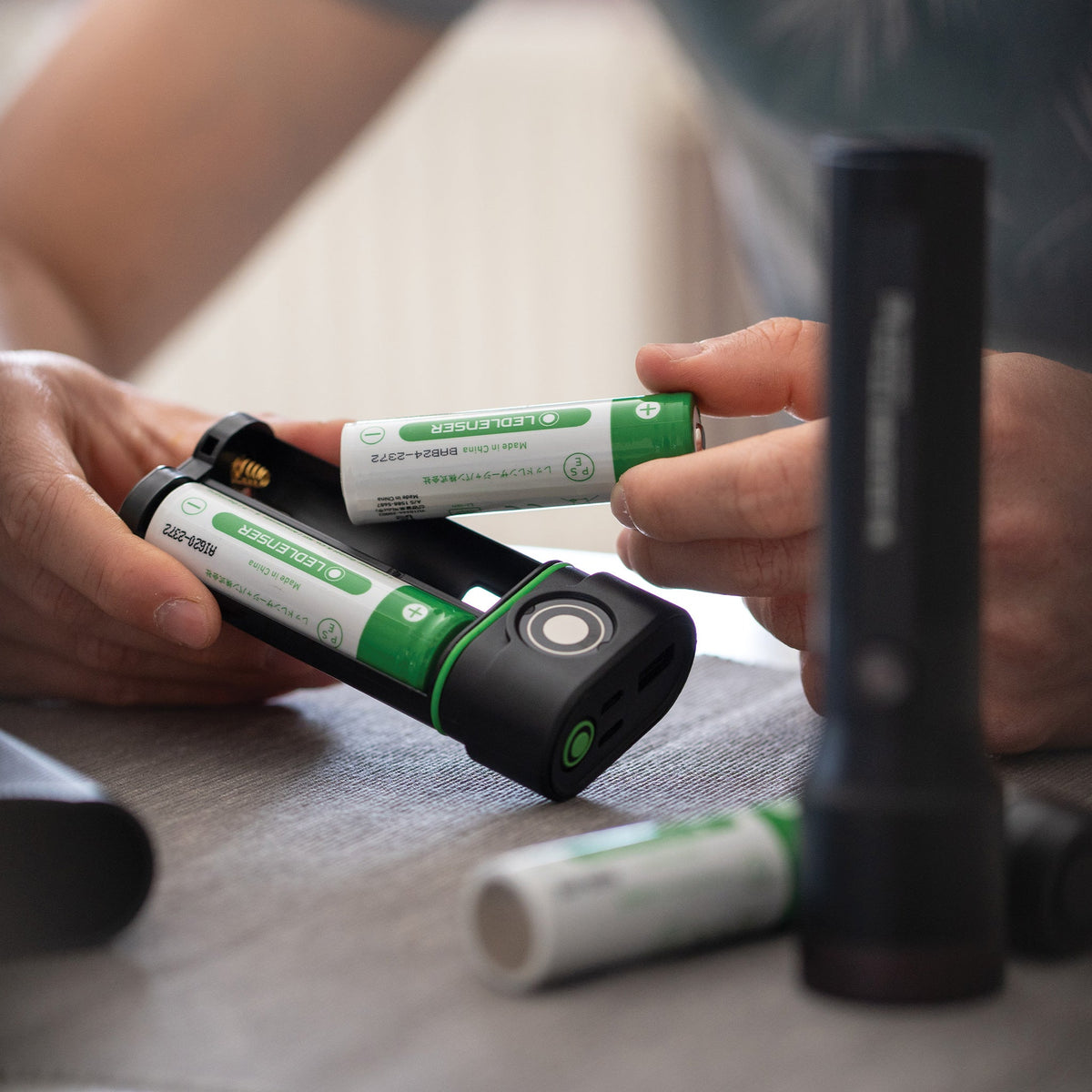Hands loading two Ledlenser 21700 batteries into the FLEX10 battery sled beside a Ledlenser torch