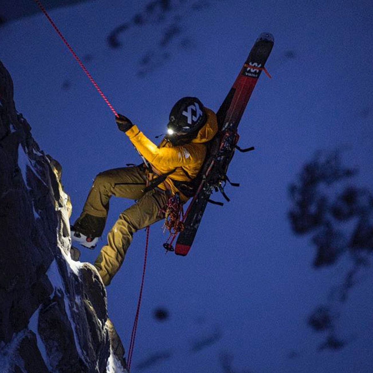 Ski mountaineer abseiling down a rock face at night wearing a Ledlenser head torch