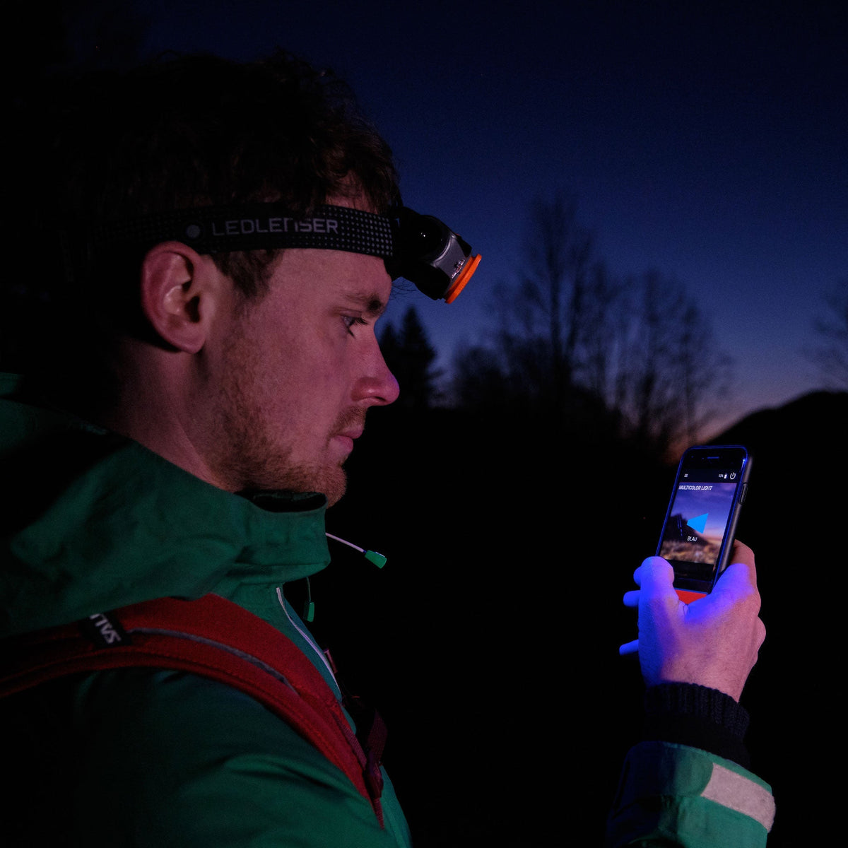 Hiker at dusk using the Ledlenser app on a phone while wearing a Ledlenser head torch