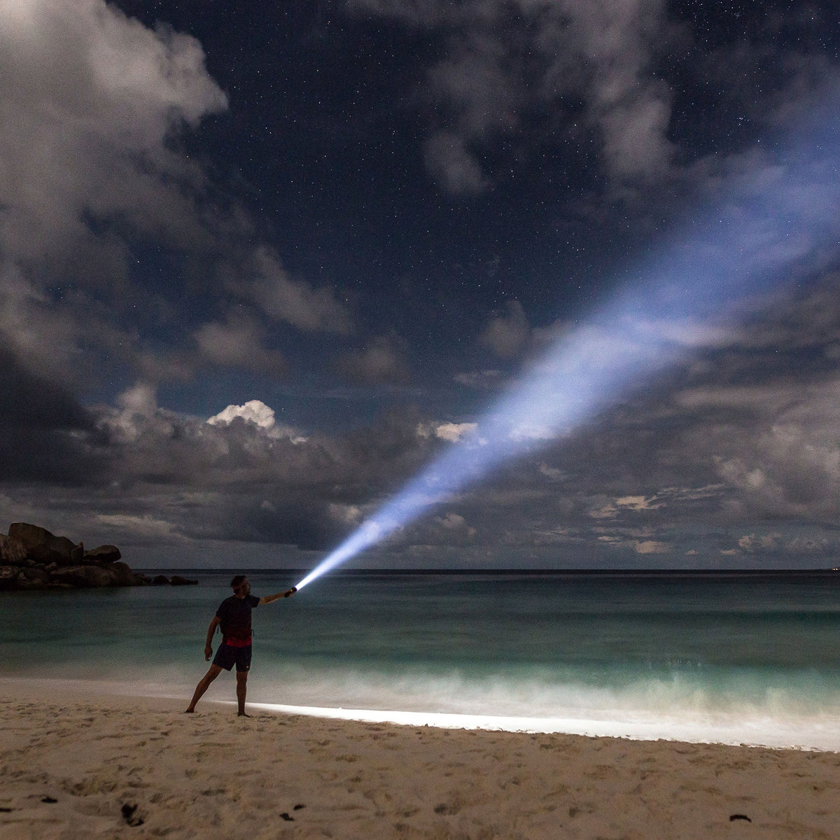 Man on a beach at night pointing the Ledlenser MT14 beam out to sea