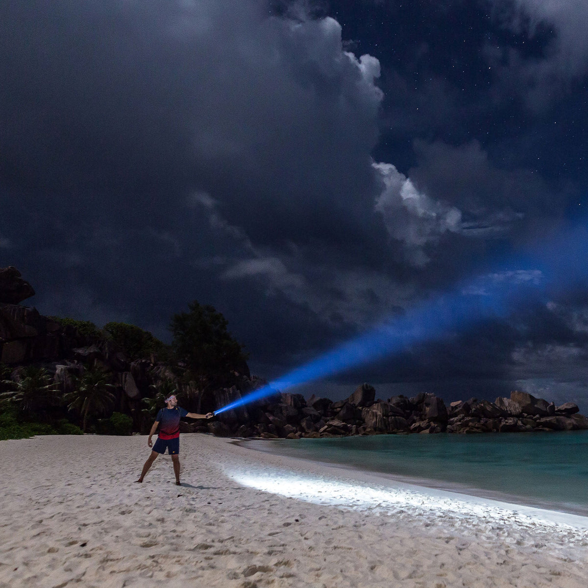 Man on a beach at night shining the Ledlenser MT14 beam into the sky