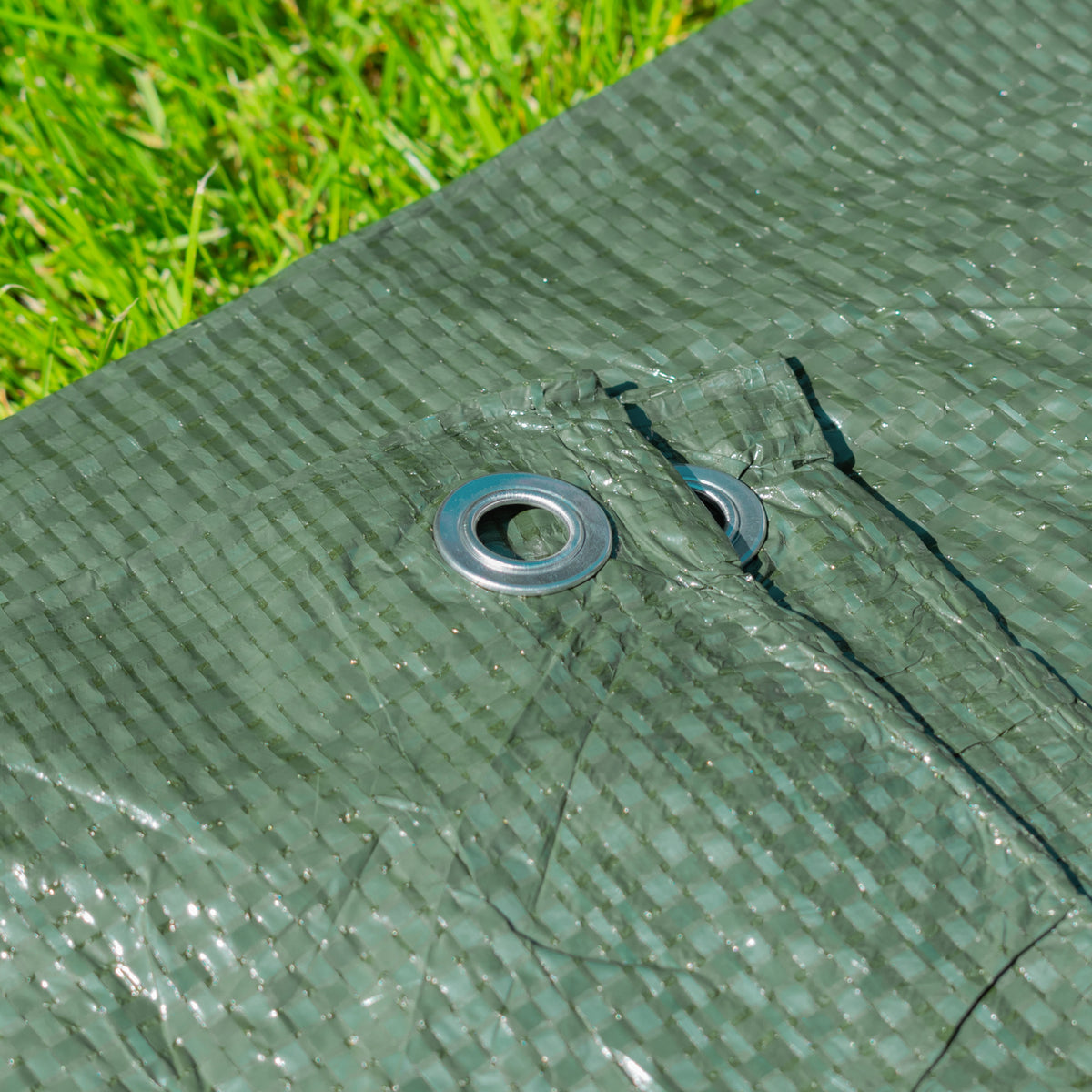 Close-up of an aluminium eyelet on the Green S-Grade Tarpaulin with 20 x 4" Bungee Balls (White) lying on grass