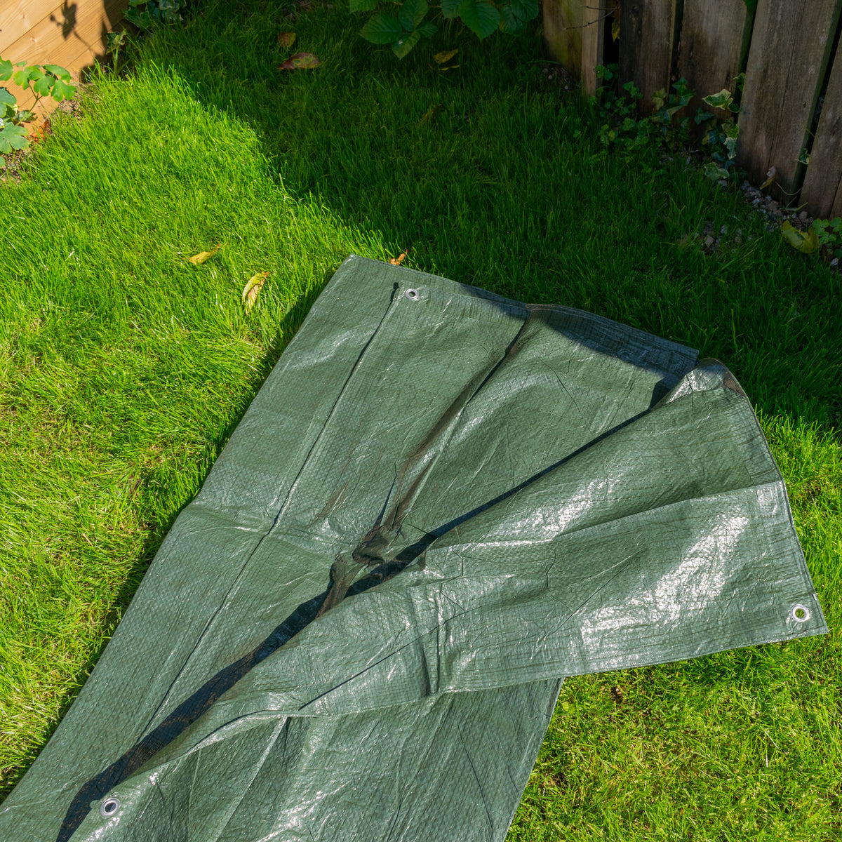 Green S-Grade Tarpaulin 3m x 5m laid out on a lawn beside a fence