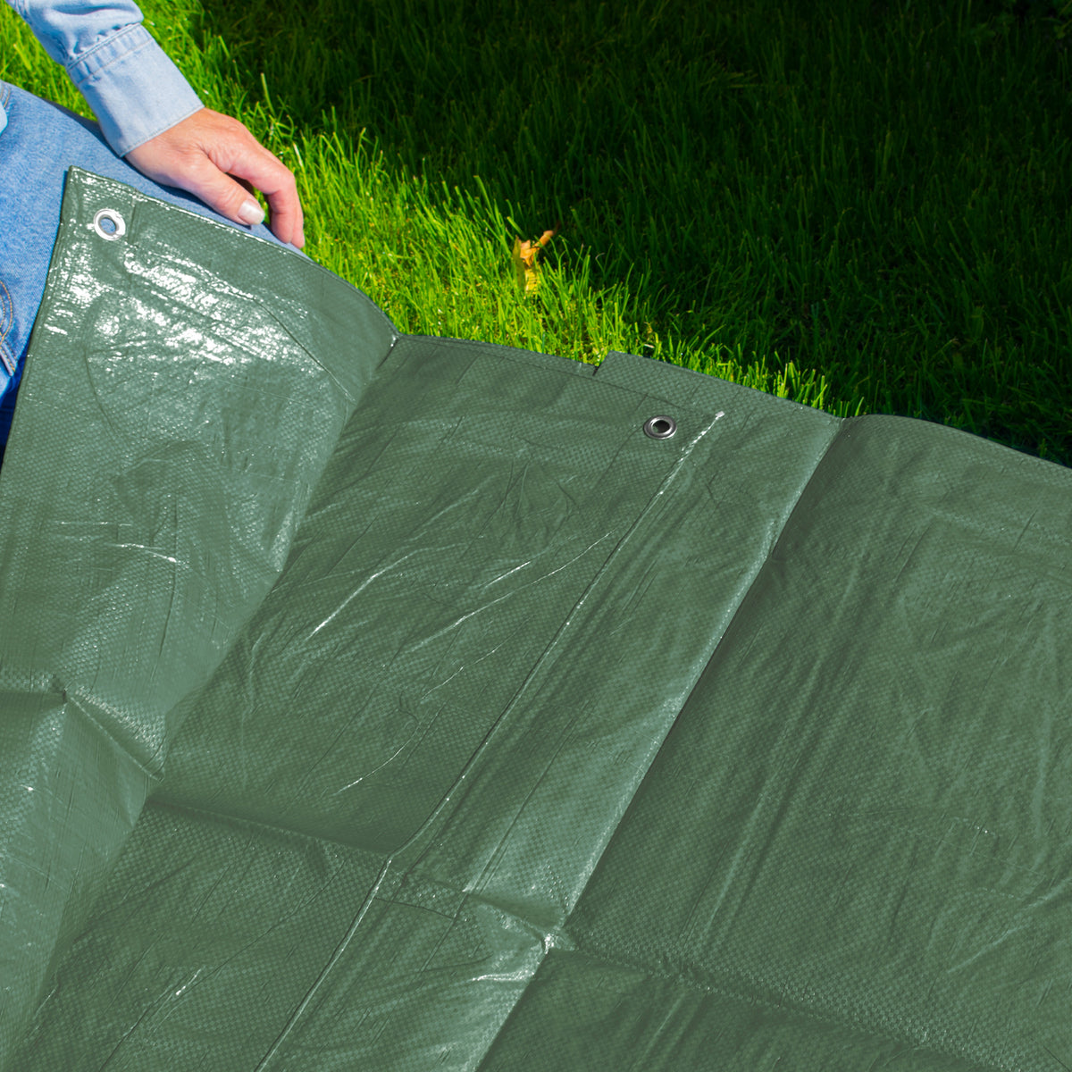Green M-Grade Tarpaulin 1.5m x 2m spread on a lawn with someone kneeling at the edge