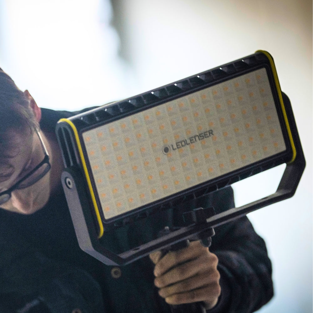 Man holding a Ledlenser AF12R Work by its bracket, the LED panel facing the camera