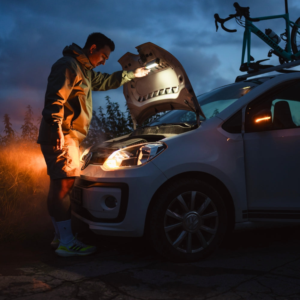 Man at the roadside at dusk lighting under the raised bonnet of a car with the Ledlenser AF2R Work