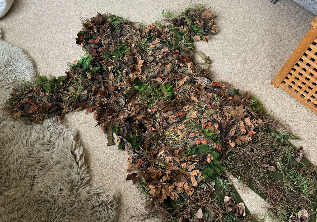 Angled close view of the leaf suit showing layered laser-cut leaves, jute strands and olive elastic loops across the hand-dyed mesh base