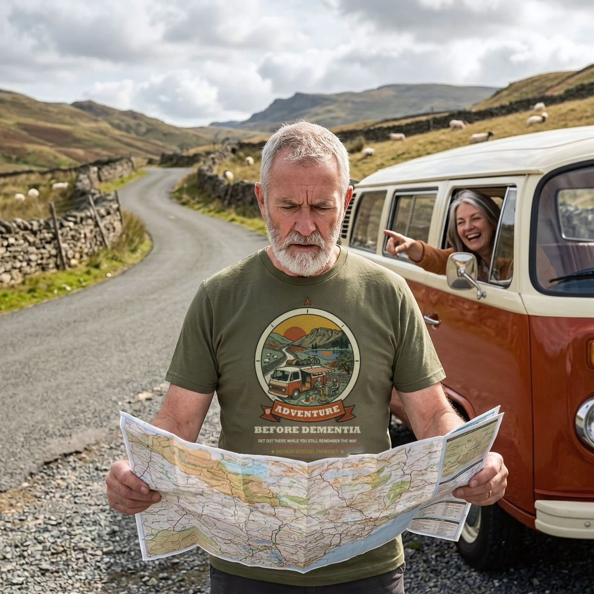 Bearded man in the Adventure Before Dementia Campervan T-Shirt in Military Green puzzling over a road map on a hill lane while his wife laughs and points from the campervan