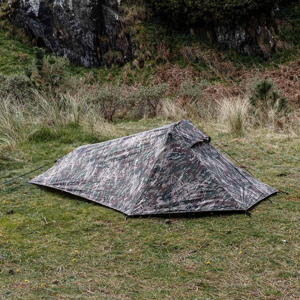 Highlander Blackthorn 1+ Tent Gen2 in HMTC Camo - pitched on grassland below a rocky crag