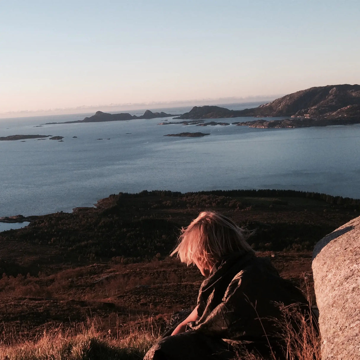 Snugpak Jungle Blanket WGTE in Olive Green wrapped around a camper on a hillside above a fjord at sunset