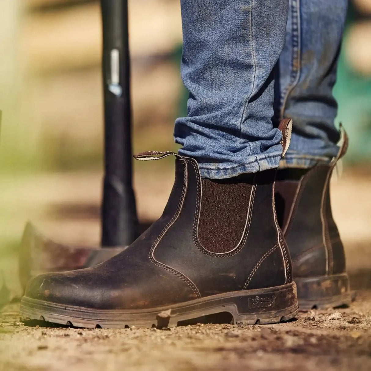 Close-up of brown Mongrel K9 dealer boots worn with jeans on a dusty farmyard track