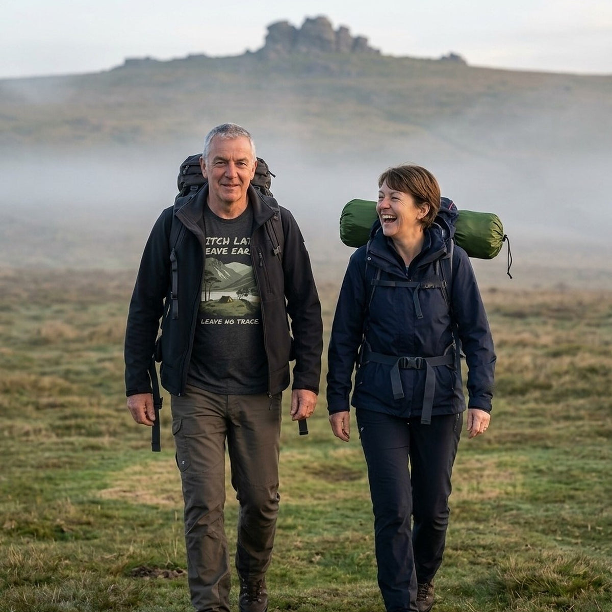 Couple walking out across Dartmoor at first light with packed rucksacks, the man wearing the Pitch Late Leave Early T-Shirt in Dark Grey Heather