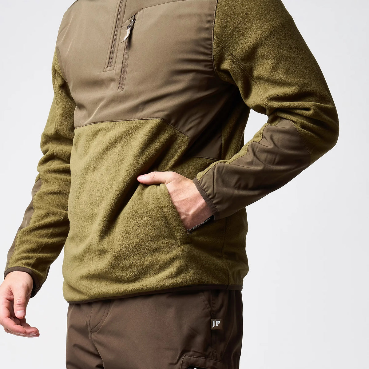 Jack Pyke Rannock Fleece Pullover in dark mustard, close-up of a hand in a zipped lower pocket beside the contrast forearm panel