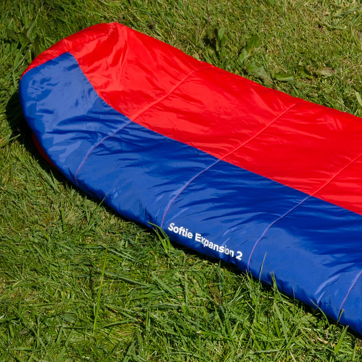 Snugpak Softie Expansion 2 WGTE Sleeping Bag in red and blue, zipped closed on grass with Softie Expansion 2 branding visible