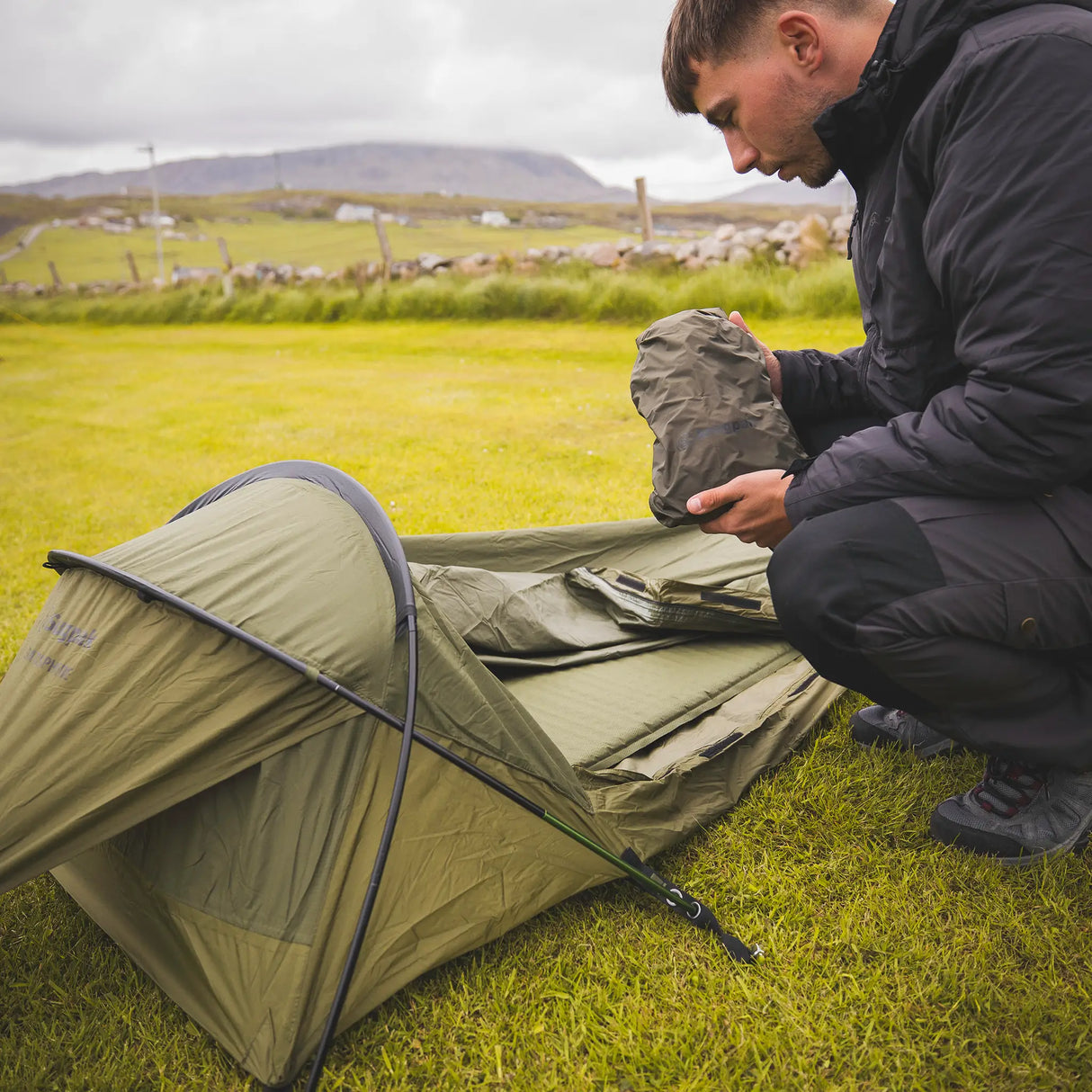 Snugpak Stratosphere WGTE Bivvi Shelter in Olive Green - camper pitching the shelter and holding the stuff sack