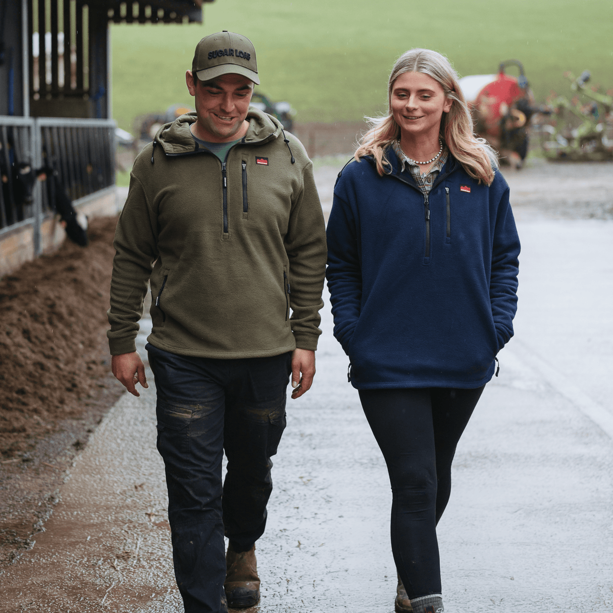 Man wearing Sugar Loaf Shepherd Polar Fleece Hoodie in Khaki walking on a path with a farm setting in the background