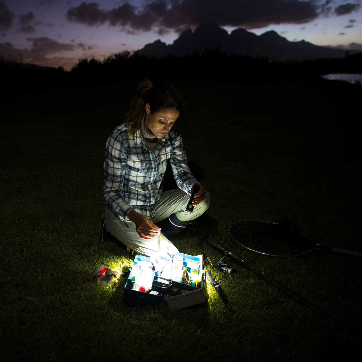 Angler sorting a tackle box on the grass at night by torchlight