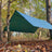DD Tarp 3.5x3.5 in olive green pitched as an A-frame shelter between trees in autumn woodland