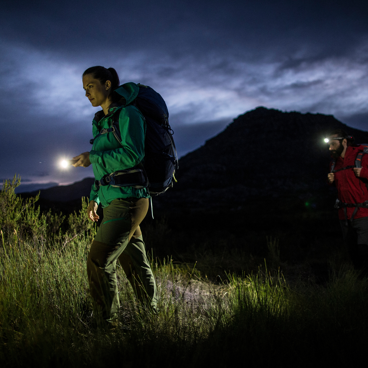 Hikers at dusk on a grassy path, one lighting the way with a Ledlenser MT10