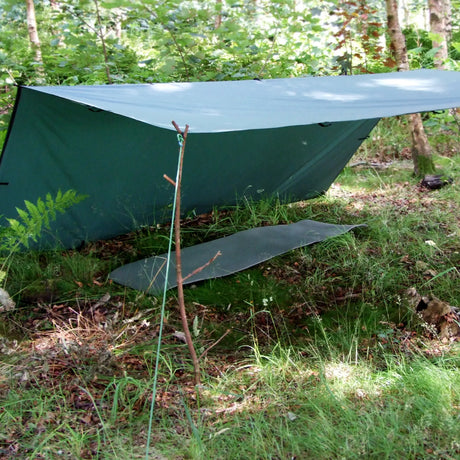 DD Tarp 3x3m in olive green pitched as a lean-to shelter over a sleeping mat in woodland