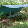 DD Tarp 3x3m in olive green pitched as a lean-to shelter over a sleeping mat in woodland