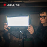 Man adjusting a lit Ledlenser AF12 floodlight on a tripod head, with the diffuser fitted