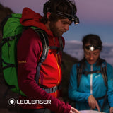 Two hikers with rucksacks reading a map at dusk under Ledlenser head torches