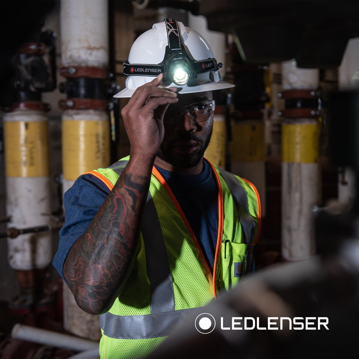 Engineer in a hard hat and hi-vis vest adjusting a Ledlenser head torch in a plant room