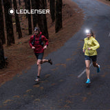 Two trail runners on a forest road at dusk wearing Ledlenser head torches