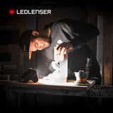 Joiner checking a sanded timber piece in a dark workshop, lit by a Ledlenser AF4R Work on the bench