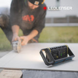 Ledlenser AF4R Work standing on a board outdoors while a tradesman cuts tile with an angle grinder