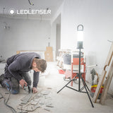 Tradesman cutting tile with an angle grinder in a stripped-out room, lit by a Ledlenser AL10R Work on a tripod