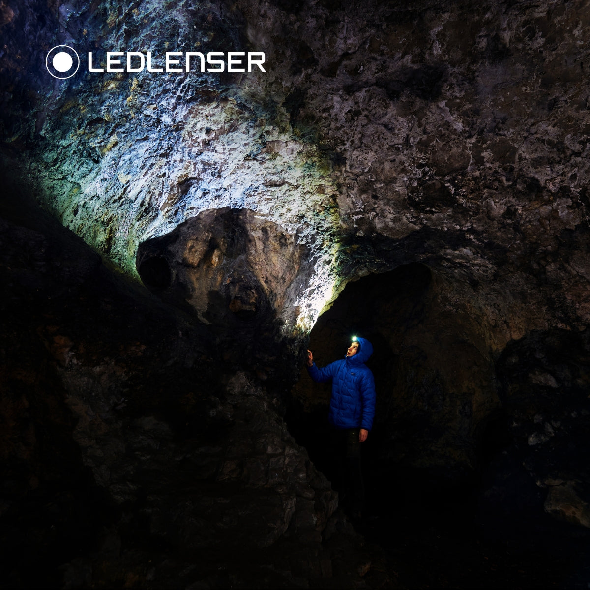 Caver in a blue jacket lighting up a rock cave with the Ledlenser MH10 SE