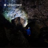 Caver in a blue jacket lighting up a rock cave with the Ledlenser MH10 SE