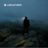 Hiker on a rocky outcrop at dusk wearing the Ledlenser MH10 SE