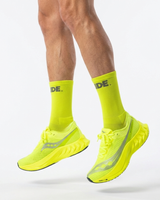 Runner mid-jump in Stride Citron Chase half crew running socks with neon yellow running shoes