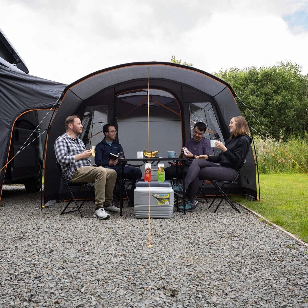 Friends sitting under the Vango Cove III front canopy beside a campervan