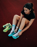 Runner sitting on a red athletics track lacing up, wearing Stride Jade Force running socks