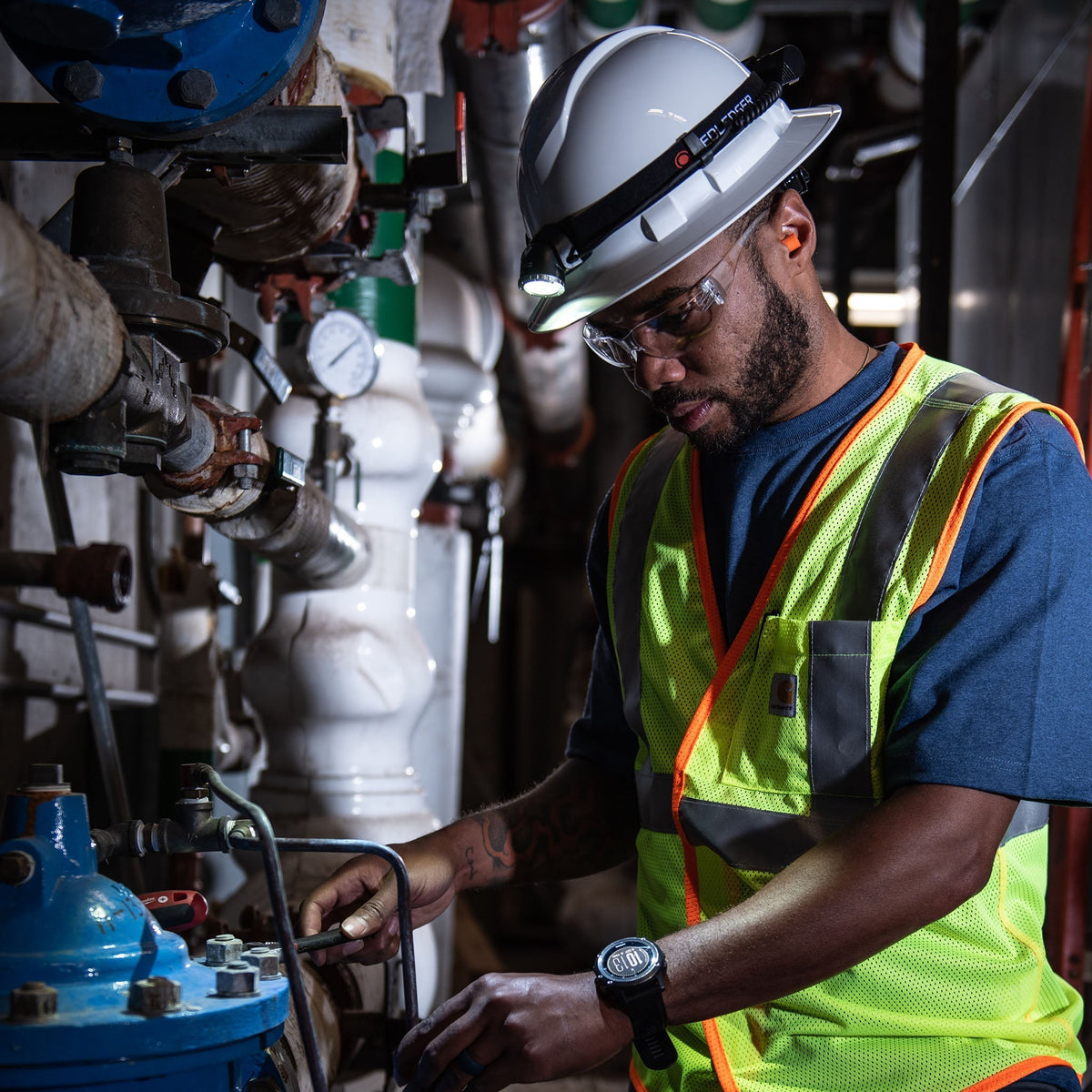 Engineer in a hard hat and hi-vis vest working on pipework with a Ledlenser head torch on the helmet