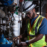 Engineer in a hard hat and hi-vis vest working on pipework with a Ledlenser head torch on the helmet