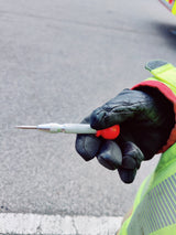 Gloved firefighter holding a spring-loaded window punch with a red cap at a roadside
