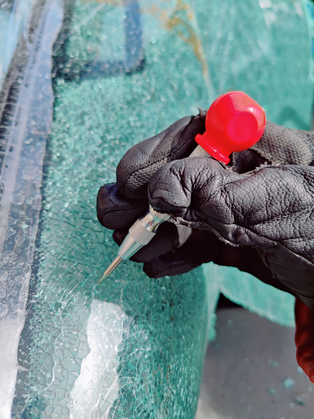 Spring-loaded window punch with red cap breaking a vehicle side window