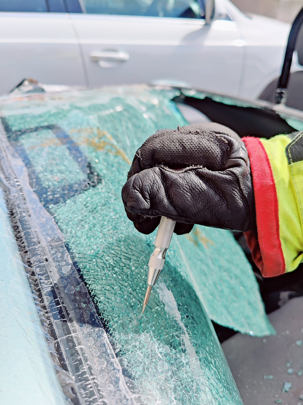 Gloved firefighter using a window punch on shattered vehicle glass